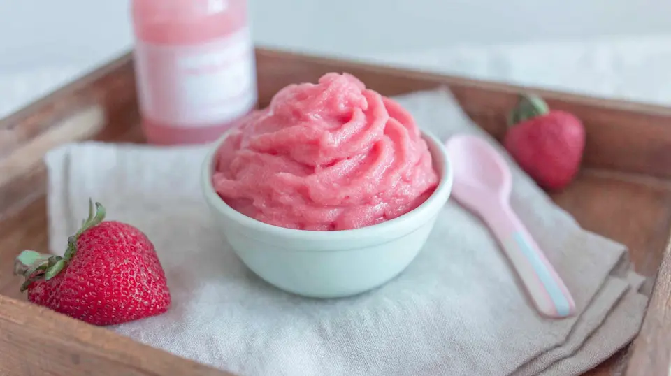 A swirl of homemade strawberry Dole Whip in a white bowl, with fresh strawberries and a pink spoon